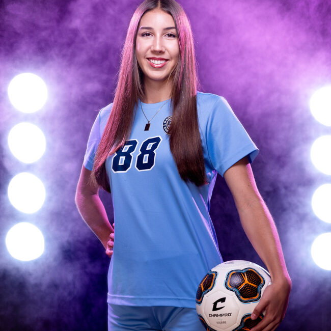 Sports photography image of girl posing with soccer ball in front of atmosphere smoke while being backlit with magenta light